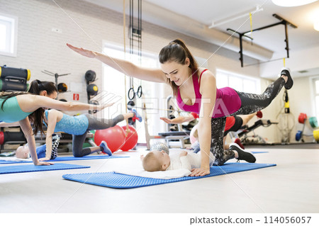 Mother smiling at baby while performing exercise above. Group exercise class, fitness or pilates for parents. Moms staying active while boding with babies. 114056057