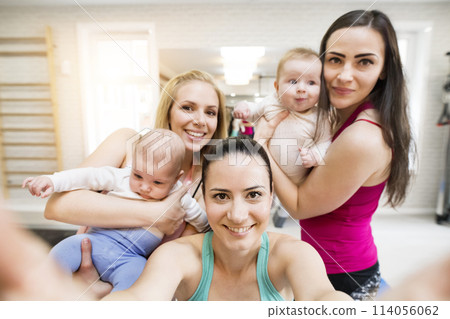 Group exercise class, mothers working out with babies in gym. Friendship between parents taking selfie. Group exercise class, mothers working out with babies in gym. Friendship between parents taking selfie. 114056062