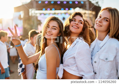 Group of happy girls at summer beach music fest, smiling, dancing in sun, flashing peace sign. Friends enjoy live concert, sunset light in background. Casual trendy outfits, fun, youth culture vibe. Group of happy girls at summer beach music fest, smiling, dancing in sun, flashing peace sign. Friends enjoy live concert, sunset light in background. Casual trendy outfits, fun, youth culture vibe. 114056260