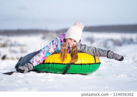 Young girl outstretched her arms while enjoying snow tubing at sunny winter weather 114056302