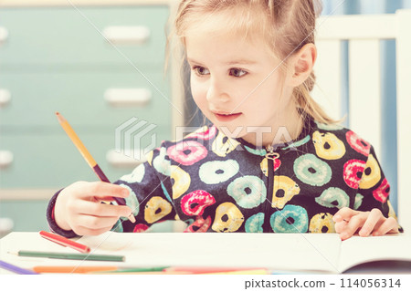 Charming blonde little girl with beauriful eyes draws with pencils and looks at camera Charming blonde little girl with beauriful eyes draws with pencils and looks at camera 114056314