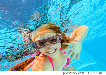 Smiling little girl in swim goggles swimming underwater in pool. Teenage girl diving underwater Smiling little girl in swim goggles swimming underwater in pool. Teenage girl diving underwater 114056380
