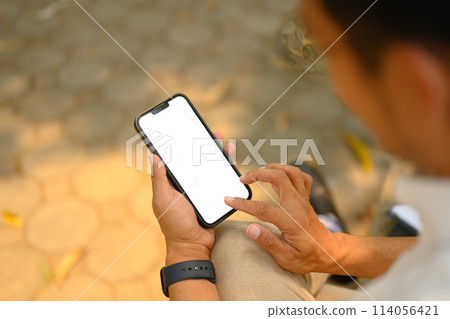 Young businessman holding smartphone with white empty screen sitting outdoor. Close up shot 114056421