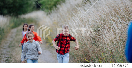 Young students having fun during biology field teaching class, running down the dirt path. Dedicated teachers during outdoor active education teaching about ecosystem, ecology. Young students having fun during biology field teaching class, running down the dirt path. Dedicated teachers during outdoor active education teaching about ecosystem, ecology. 114056875