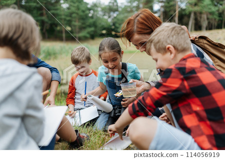 Young students analyzing water quality, ph level with indicator strips during biology field teaching class. Female teacher during outdoor active education. 114056919