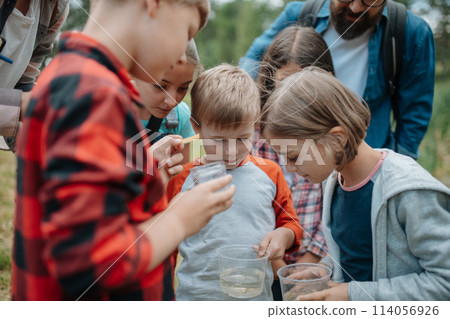 Young students analyzing water quality, ph level with indicator strips during biology field teaching class. Female teacher during outdoor active education. 114056926