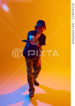 Young stylish man, lost in the rhythm, raps with precision and flow, creating mesmerizing sounds against yellow background in neon light 114059119