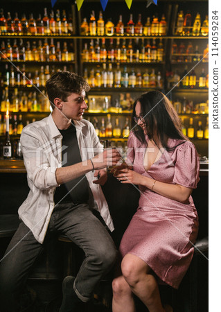 Handsome guy treats lady with glasses to cocktail in bar Handsome guy treats lady with glasses to cocktail in bar 114059284
