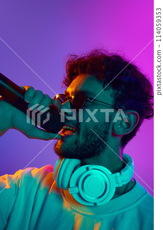 Close-up of young man in sunglasses, with microphone performing rap against gradient pink purple background in neon light Close-up of young man in sunglasses, with microphone performing rap against gradient pink purple background in neon light 114059353