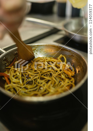 Skilled cook stirs noodles with mix of vegetables in pan Skilled cook stirs noodles with mix of vegetables in pan 114059377