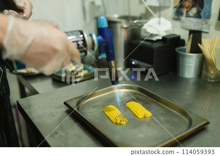 Cook grills sweet corn with handy gas burner in kitchen 114059393