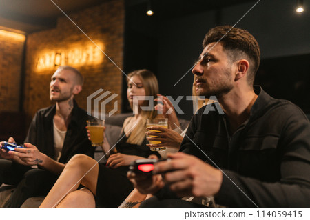 Women sit among men playing console games in game room 114059415