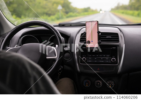 Rear view of a young traveler using a navigator on a mobile phone behind the wheel of a modern car . 114060206