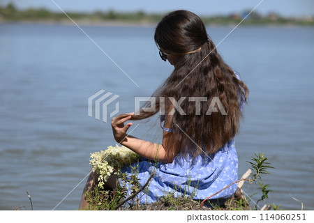 A young girl with long dark hair stands on the bank of the river. A young girl with long dark hair stands on the bank of the river. 114060251