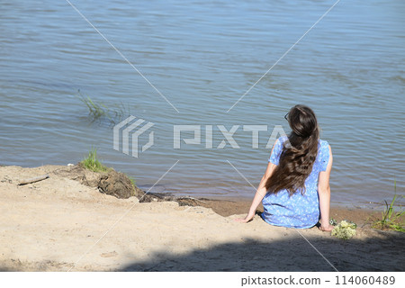 A young girl with long dark hair stands on the bank of the river. 114060489