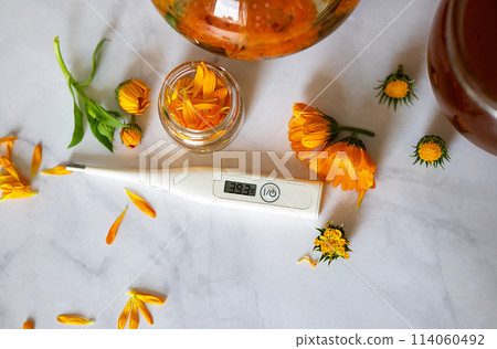 Cup of marigold tea and calendula flowers outdoors on green background. Cup of marigold tea and calendula flowers outdoors on green background. 114060492