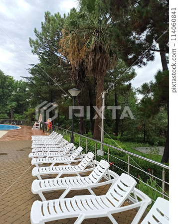 The deck chairs are empty, standing in a row, near the pool. 114060841