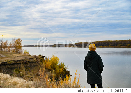 A girl in a yellow jacket and a dark jacket looks at an autumn leaf 114061141