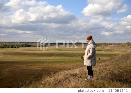 A girl in a light jacket and a brown hat looks at the autumn landscape A girl in a light jacket and a brown hat looks at the autumn landscape 114061241