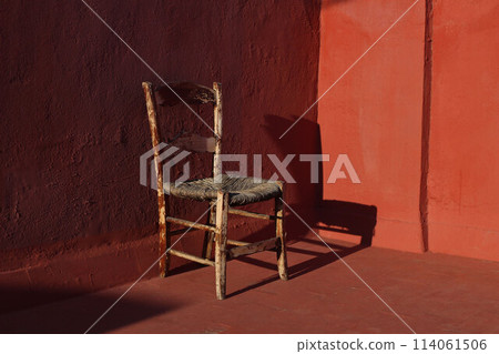 Old wooden one vintage chair in a room with red grunge walls and floor in sunlight, dark shadows. Shabby antique furniture. Empty copy space, no people. Retro interior still life, concept. 114061506