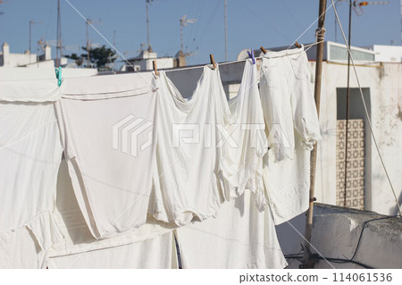 White various clothes hanging and drying in wind on rope. Laundry with clothes pins on line outdoors. Spanish rooftop. Summer Mediterranean still life, city life. No people. 114061536