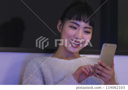 Young woman looking at smartphone screen at night at home 114062103