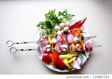 Crude kebab skewers on a chopping board with vegetables and spices on wooden rustic Raw skewers of meat. Barbecue meat with vegetables and spices on a stone background. Free space for your text. 114062553