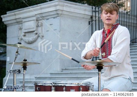masterfully play drum beautiful young guy of European appearance in Ukrainian embroidered shirt national clothes of Ukraine plays drum waving sticks power of happiness professional musician fast play 114062685