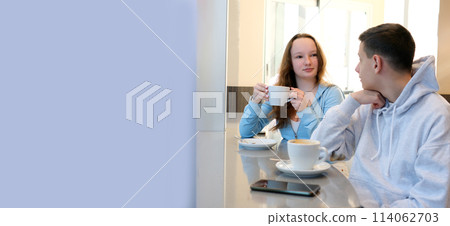 young people boy girl sitting in a cafe teen chatting drinking coffee white cup in hand laughing having fun spending time together student canteen restaurant cafe school sit by window white frame 114062703