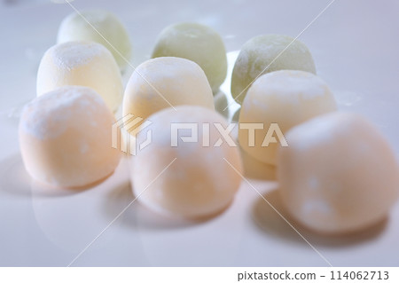 different flavors of Asian dessert mochi, a woman hand takes out sweet ice cream made from peas and rice starch dough from a box onto a white plate different flavors of Asian dessert mochi, a woman hand takes out sweet ice cream made from peas and rice starch dough from a box onto a white plate 114062713