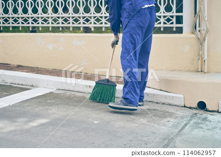 The janitor sweeps the parking space next to the store with a broom. Cleaning the city, streets from dust and dirt. High quality photo 114062957