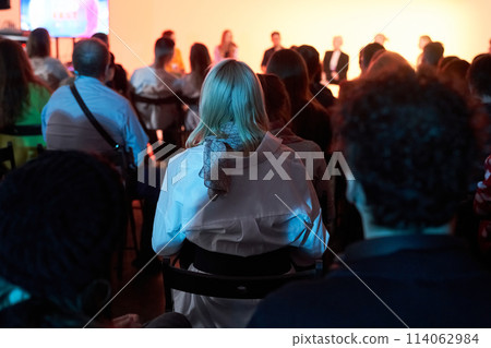 Background of unrecognizable people standing with their backs to the camera and facing the stage where the speakers are speaking. Business event. High quality photo 114062984