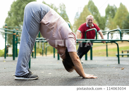 Mature woman doing yoga outdoors in city sports ground Mature woman doing yoga outdoors in city sports ground 114063034