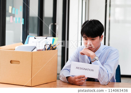 Man at desk with resignation letter, pondering his decision beside a packed box. Man at desk with resignation letter, pondering his decision beside a packed box. 114063436