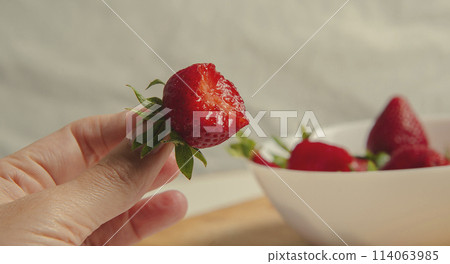 Close-up of strawberries in a woman hands against the background of strawberries in a bowl Close-up of strawberries in a woman hands against the background of strawberries in a bowl 114063985