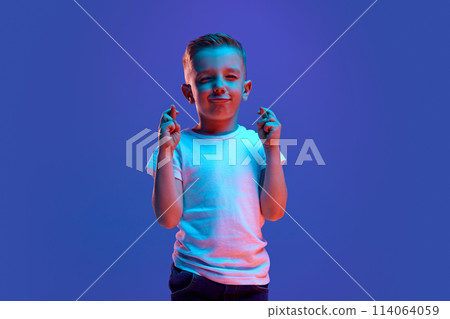 Good luck at exam. Cute child, boy crossed fingers and closed eyes to get lucky in mixed neon light against blue background. Good luck at exam. Cute child, boy crossed fingers and closed eyes to get lucky in mixed neon light against blue background. 114064059