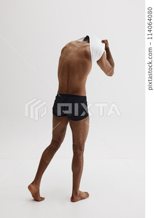 Full-length image of muscular young man i underwear taking off t-shirt, showing athletic body isolated on white background 114064080