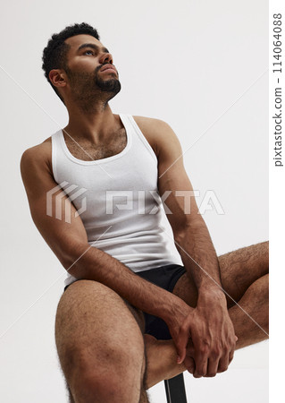 Young bearded handsome African-American man with athletic, muscular body sitting on char with thoughtful face isolated on white background 114064088