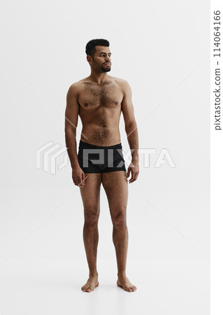 Full-length image of handsome African-American man standing shirtless in black boxes isolated on white background. Masculinity 114064166