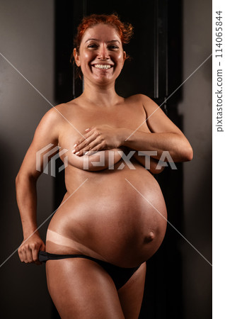 Pregnant woman pulls back her panties showing instant tan. Vertical photo.  114065844