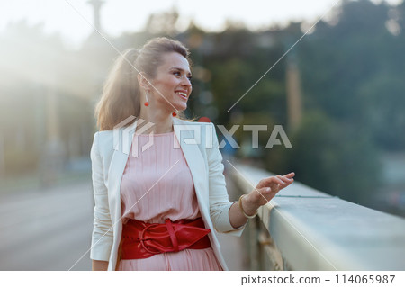 smiling stylish woman in pink dress and white jacket in city 114065987