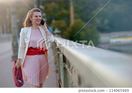 smiling woman in dress and jacket in city using phone 114065989