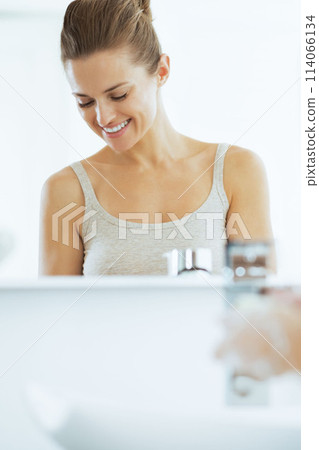 Happy young woman washing hands in bathroom 114066134