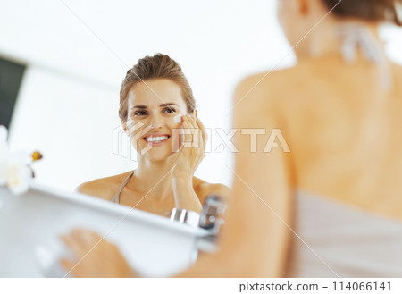 Happy young woman applying cream in bathroom 114066141