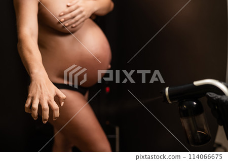 The master applies bronzer with a spray on the hands of a pregnant woman. Instant tan.  114066675