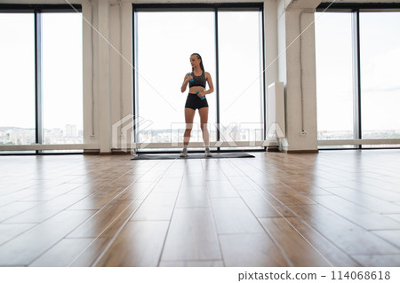 Fit young woman wearing workout gear stands on mat. 114068618
