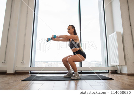 Young woman exercising with dumbbells in a bright gym Young woman exercising with dumbbells in a bright gym 114068620