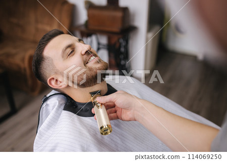Hairdresser cutting hair on beard of a handsome man Hairdresser cutting hair on beard of a handsome man 114069250