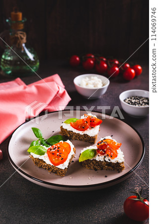 Appetizing crostini on rye bread with ricotta and tomatoes on a plate vertical view Appetizing crostini on rye bread with ricotta and tomatoes on a plate vertical view 114069746