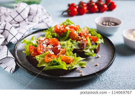 Bruschetta on rye bread with lettuce, tomatoes and sesame on a plate on the table Bruschetta on rye bread with lettuce, tomatoes and sesame on a plate on the table 114069767
